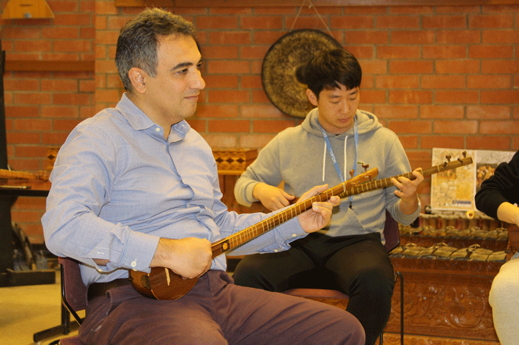 Two men play stringed Iranian instruments in a classroom.