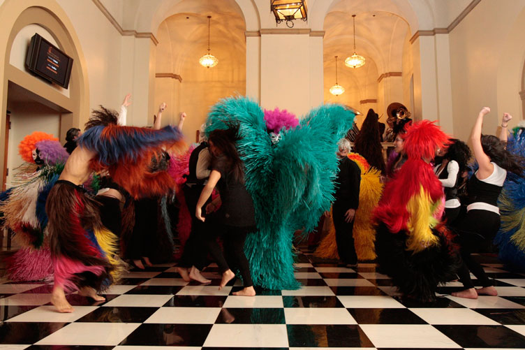 Performers in feathered costumes dance in Royce Hall’s lobby.