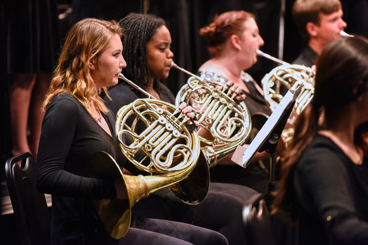 Three young women play French horns in an orchestra.