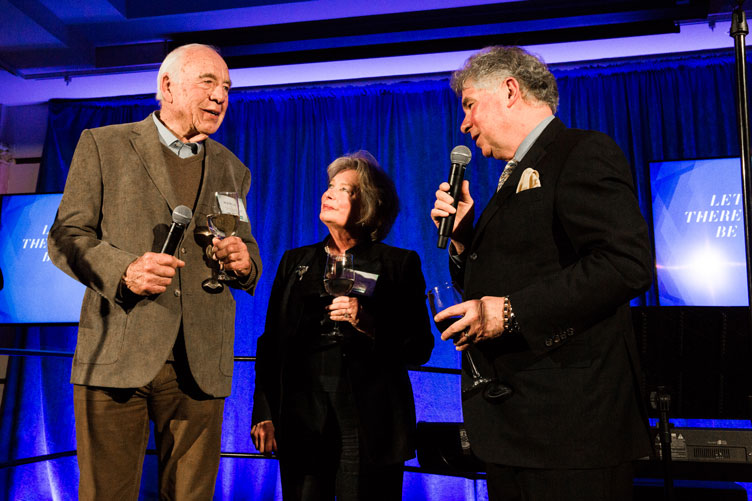 Three donors stand onstage to give a celebratory toast.