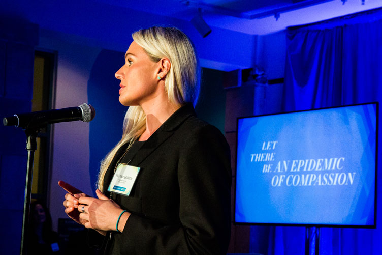 Speaker shares her thoughts onstage with the segment title “Let There Be an Epidemic of Compassion” on the screen behind her.