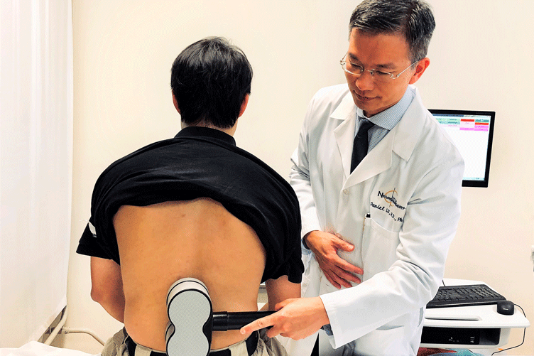 Dr. Daniel Lu treats a patient by holding a magnetic device over the lumbar spine at the lower back.