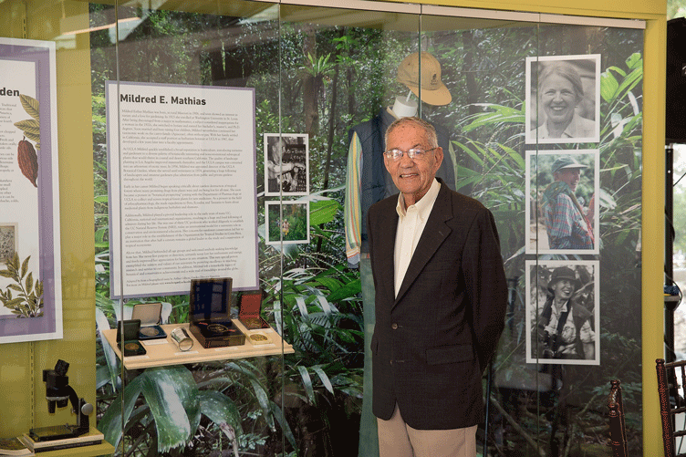 La Kretz stands in front of a display featuring information, photos, and memorabilia related to Mildred E. Mathias.