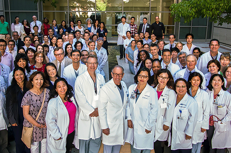 Dr. Busuttil and dozens of medical staff pose outdoors in a building courtyard.