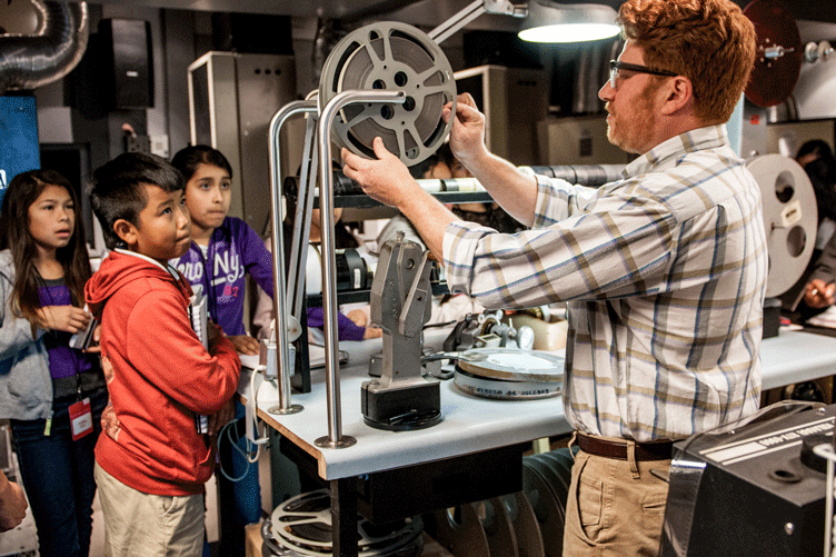 Teacher shows a group of young students a film reel.