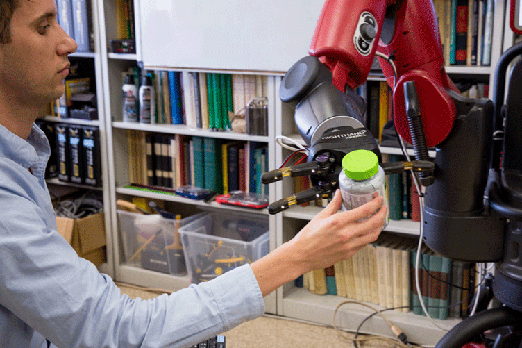 Student holds up a container for a robot to grab with its claw.