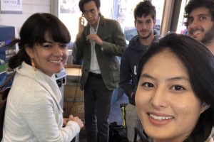 Two women and two men stand in an office and smile at the camera while a third man looks off to the side