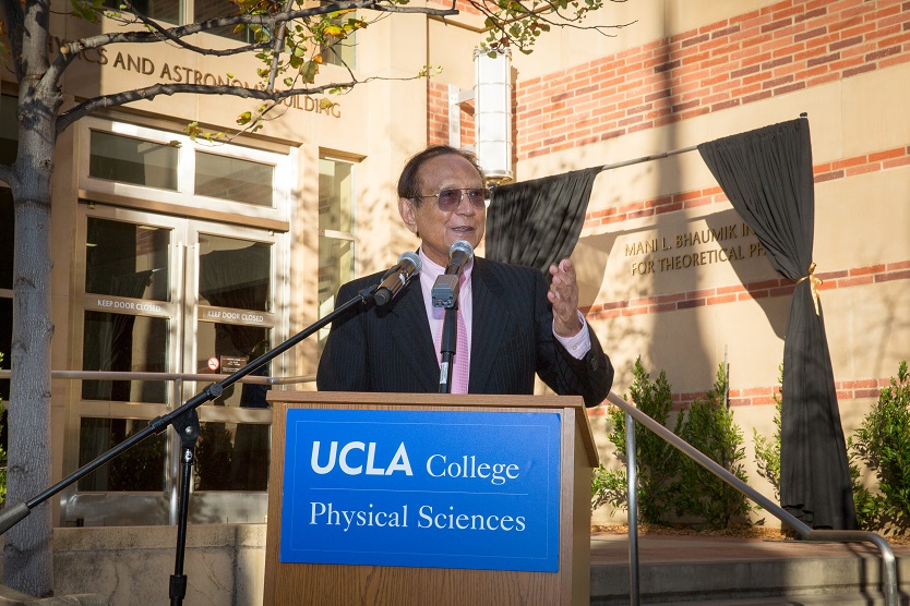 Older man with medium-dark skin gestures while speaking from a podium outside.