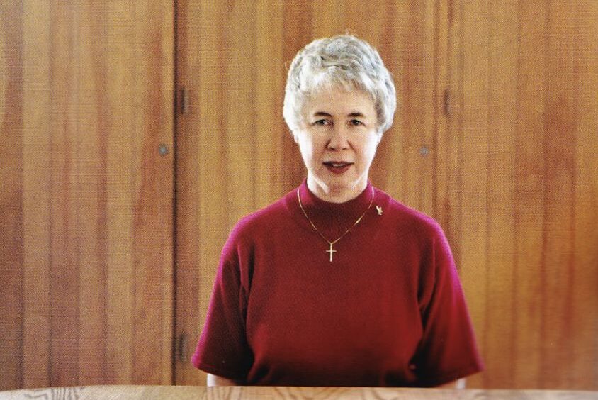 A woman (April Moell) in a burgundy sweater sits before a wooden wall.
